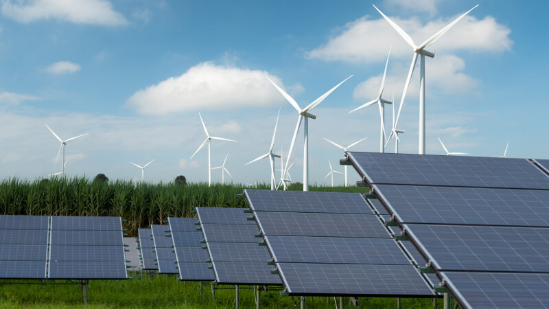 A set of wind turbines and solar panels in a large green field